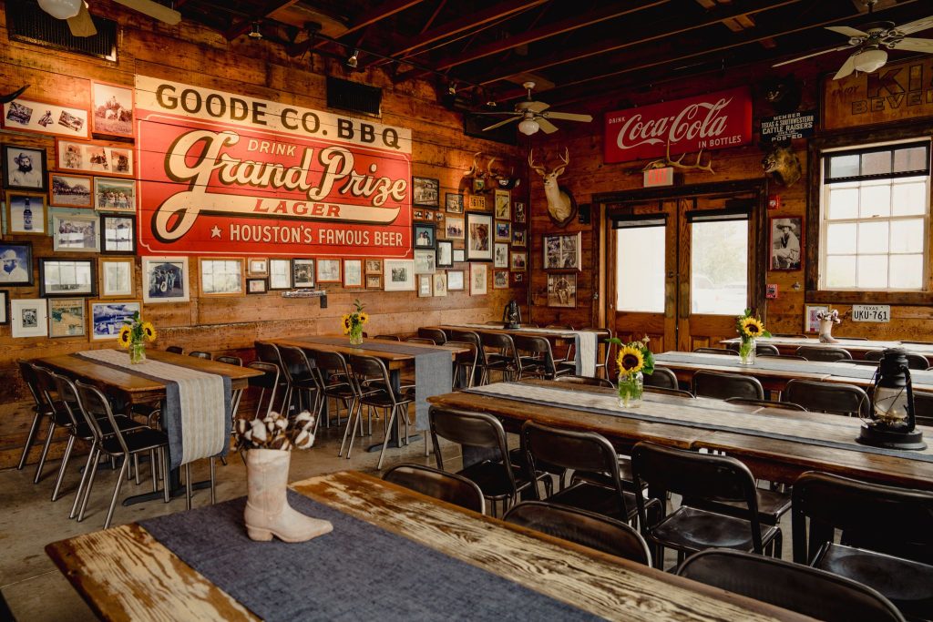 Inside of Goode Co. BBQ restaurant with long wooden tables decorated with sunflowers in small vases.