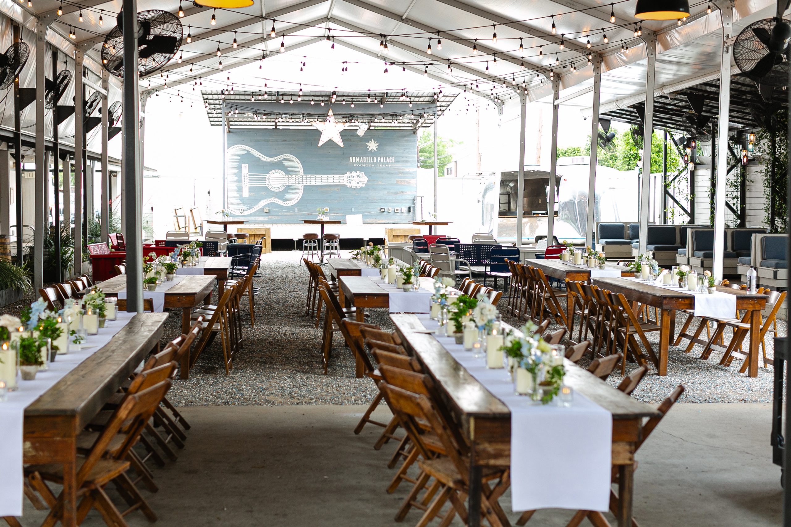 White table runners lining brown wooden tables decorated with lit candles and flowers, with the Armadillo Palace sign hanging at the back of the stage.